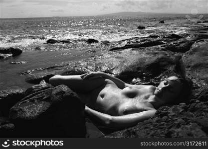 Mid adult nude Caucasian woman laying in water at Maui, Hawaii beach with eyes closed.