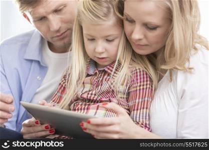 Mid adult parents using tablet PC with daughter at home
