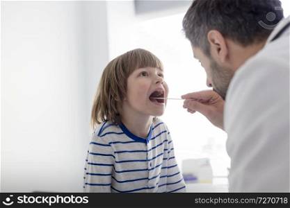 Mid adult pediatrician checking boy patient with depressor at hospital