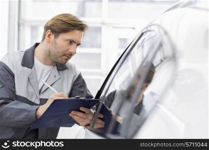Mid adult repair worker writing on clipboard while examining car in workshop