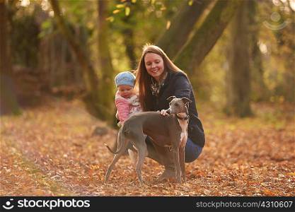 Mid adult woman and baby daughter petting dog in autumn park