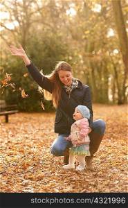 Mid adult woman and baby daughter watching autumn leaves in park