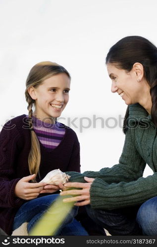 Mid adult woman and her daughter holding a conch shell and smiling
