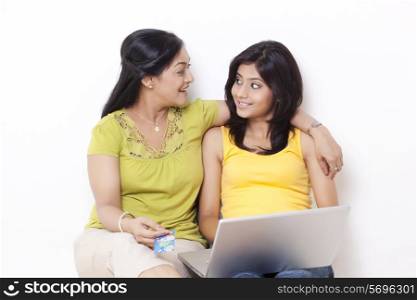 Mid adult woman and her daughter looking at each other while shopping online