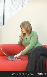 Mid adult woman eating a cookie and working on a laptop