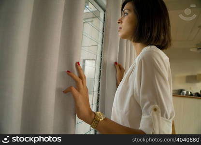 Mid adult woman gazing out of curtained window