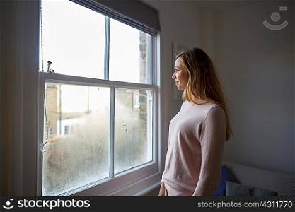 Mid adult woman gazing out through bedroom window