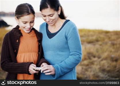 Mid adult woman holding a digital camera and standing with her daughter