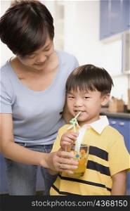 Mid adult woman holding a glass of juice and her son drinking from it