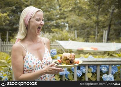 Mid adult woman holding a plate of roast chicken and shouting
