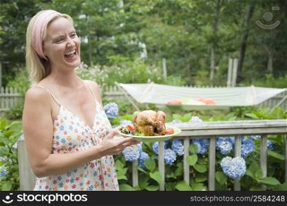Mid adult woman holding a plate of roast chicken and smiling