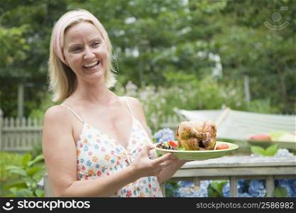 Mid adult woman holding a plate of roast chicken and smiling