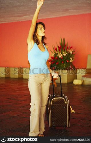 Mid adult woman holding a suitcase with her hand raised