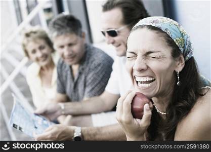 Mid adult woman holding an apple with her friends sitting beside her