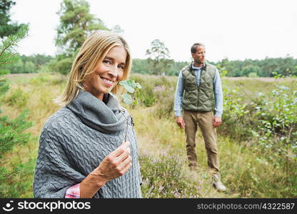 Mid adult woman holding leaf, man in background