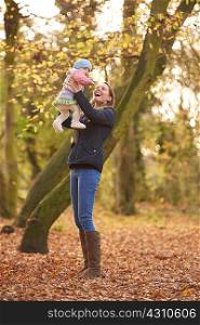 Mid adult woman holding up baby daughter in autumn park
