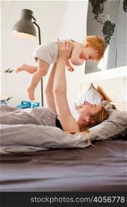 Mid adult woman holding up baby daughter in bed
