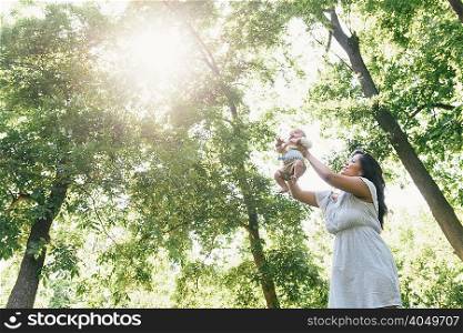 Mid adult woman holding up baby son in Pelham Bay Park, Bronx, New York, USA