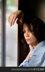 Mid-adult woman in man's shirt leans on window frame
