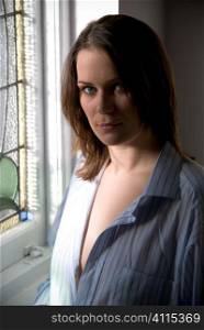 Mid-adult woman in man's shirt next to window frame