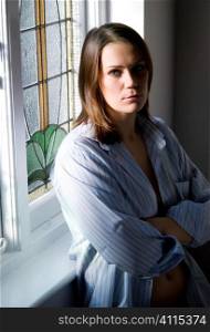 Mid-adult woman in man's shirt next to window frame