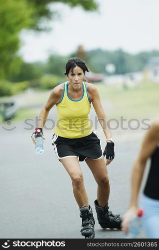 Mid adult woman inline skating and holding a water bottle