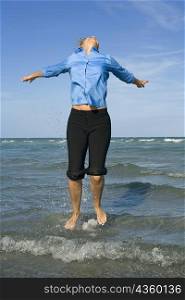 Mid adult woman jumping on the beach with her arms outstretched