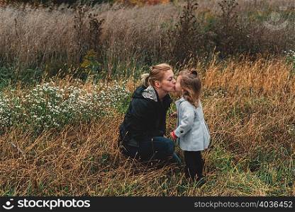 Mid adult woman kissing toddler daughter in field of long grass