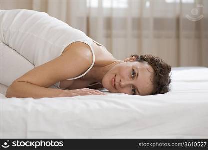 Mid adult woman kneels on bed smiling at camera