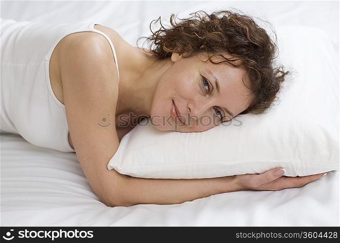 Mid adult woman lies on pillow smiling at camera