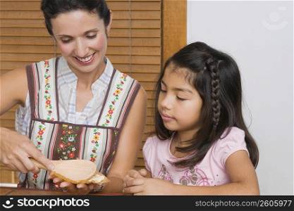 Mid adult woman preparing bread with her daughter in the kitchen