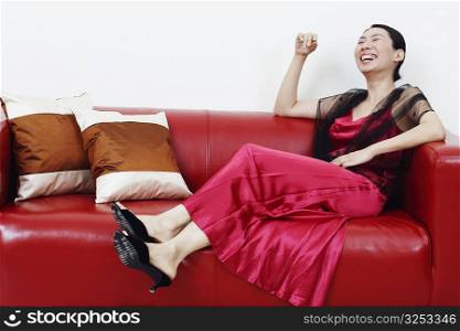Mid adult woman reclining on a couch and laughing with her eyes closed