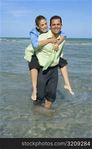 Mid adult woman riding piggyback on a mid adult man on the beach