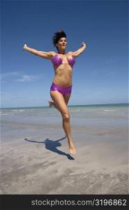 Mid adult woman running on the beach with her arms outstretched
