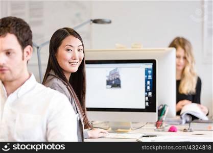 Mid adult woman sitting at computer looking over shoulder at camera smiling