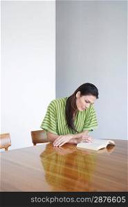 Mid adult woman sitting at table reading book