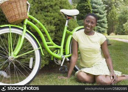 Mid adult woman sitting beside a bicycle and smiling