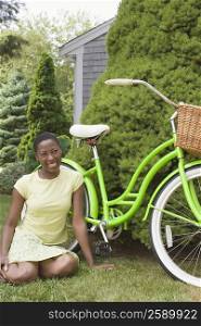 Mid adult woman sitting beside a bicycle and smiling