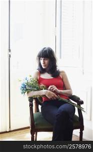 Mid adult woman sitting in an armchair and holding a bunch of flowers