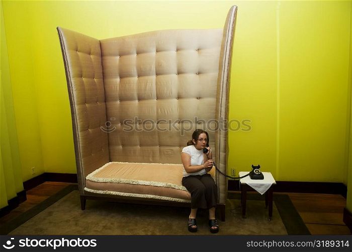 Mid adult woman sitting in an armchair and talking on a rotary phone