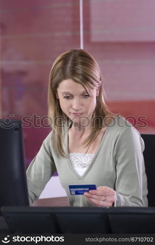 Mid adult woman sitting in front of a computer and holding a credit card