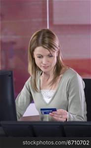 Mid adult woman sitting in front of a computer and holding a credit card