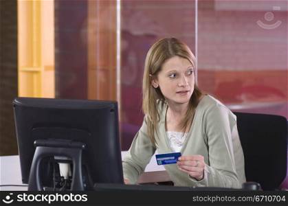 Mid adult woman sitting in front of a computer and holding a credit card