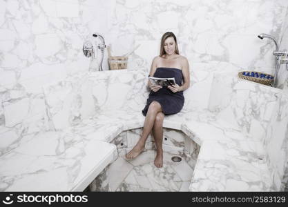 Mid adult woman sitting in the bathroom and reading a magazine