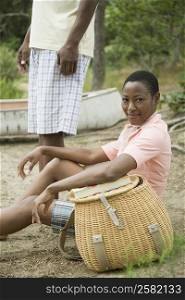 Mid adult woman sitting near a picnic basket with a mature man standing beside her