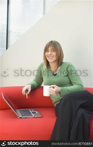 Mid adult woman sitting on a couch with a laptop beside her