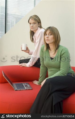 Mid adult woman sitting on a couch with another woman sitting behind her