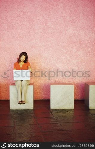 Mid adult woman sitting on a cube seat and holding a laptop