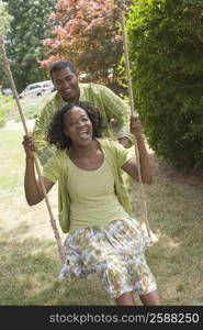 Mid adult woman sitting on a rope swing with a mature man pushing her