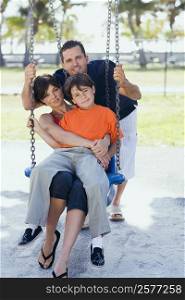 Mid adult woman sitting on a swing with her son and a mid adult man pushing them